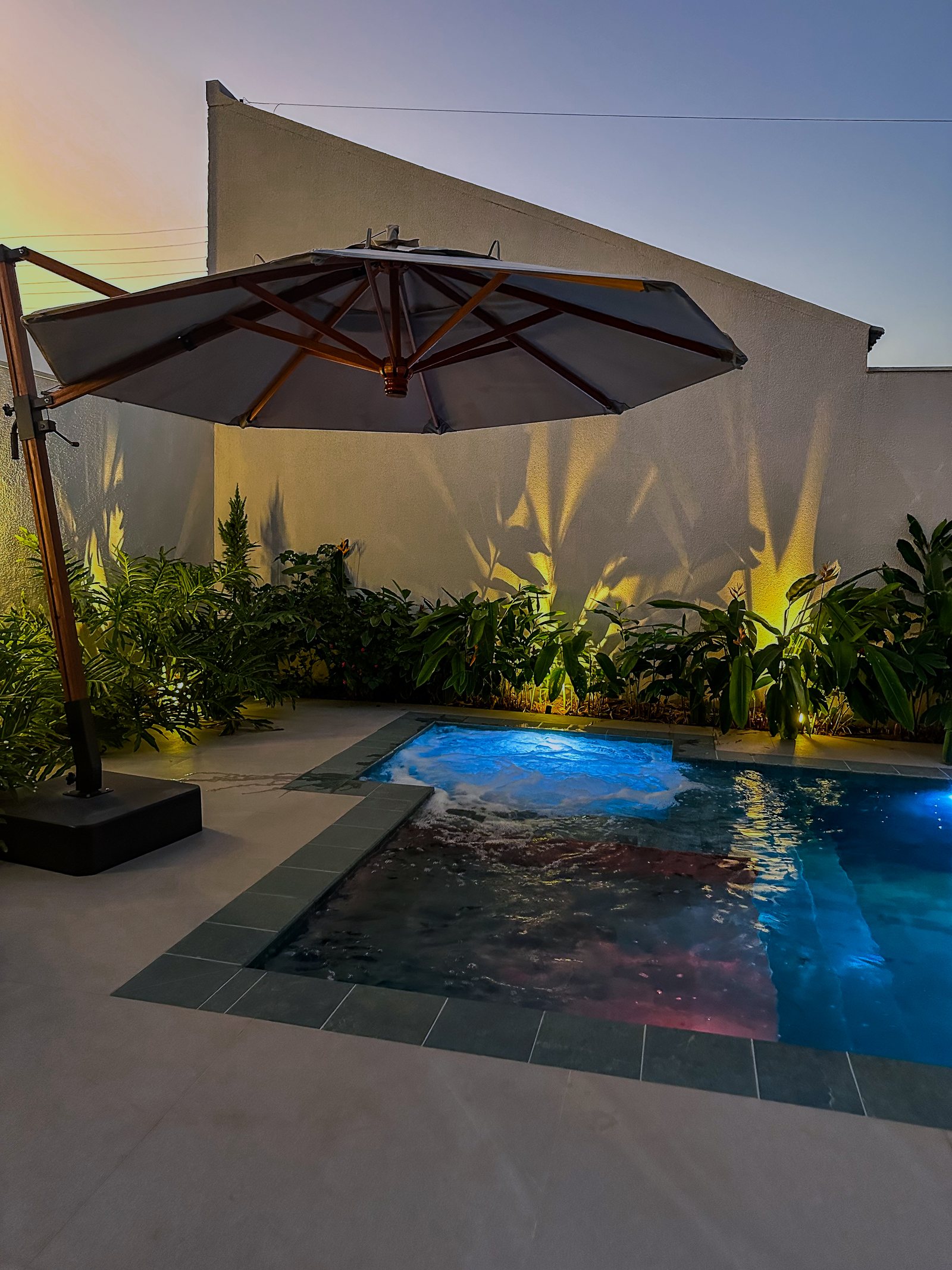 Piscina noturna com guarda-sol e iluminação de paisagismo